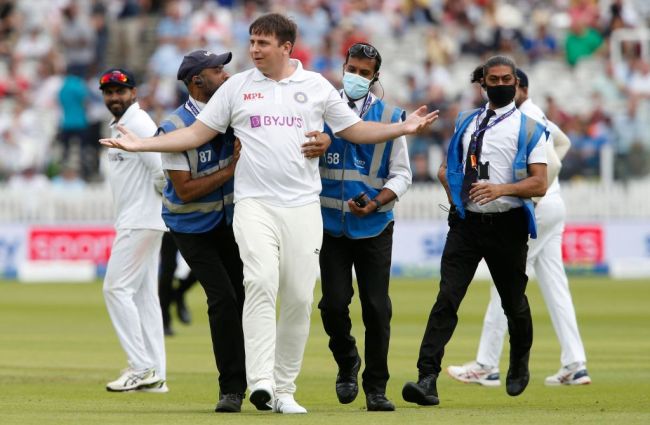 A pitch invader is escorted off of the the pitch on the third day of the second cricket Test match between England and India at Lord's cricket ground in London on August 14, 2021.