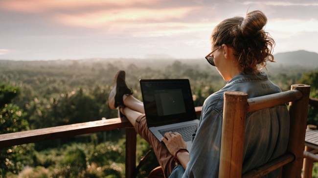Young business woman working at the computer in cafe on the rock. Young girl downshifter working at a laptop at sunset or sunrise on the top of the mountain to the sea, working day