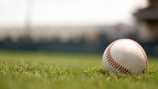 A ball lays in the outfield grass of a baseball field.