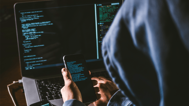 hacker looking at phone and laptop